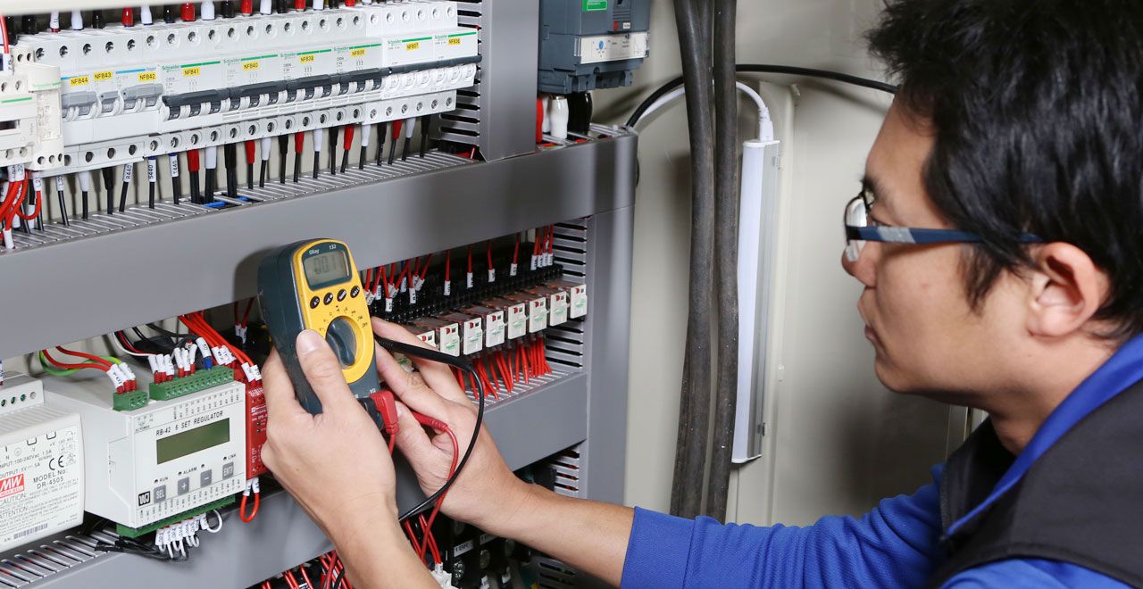 Technician testing an electrical control panel with a multimeter.